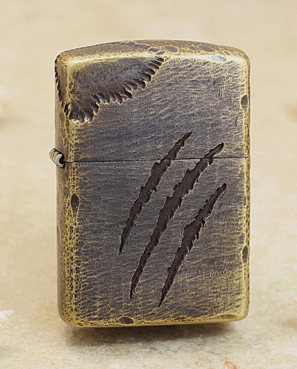 Leather-wrapped Zippo-style lighter with three claw-mark scratches on the front piece, on a sandy surface.