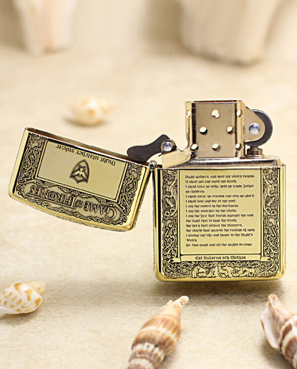 KZ196-02 Ornate gold lighter open on a sandy beach, surrounded by seashells, showcasing intricate engravings and text panels.