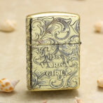 Gold-tone lighter with intricate scrollwork engraving reading '1935 VARGA GIRL'.