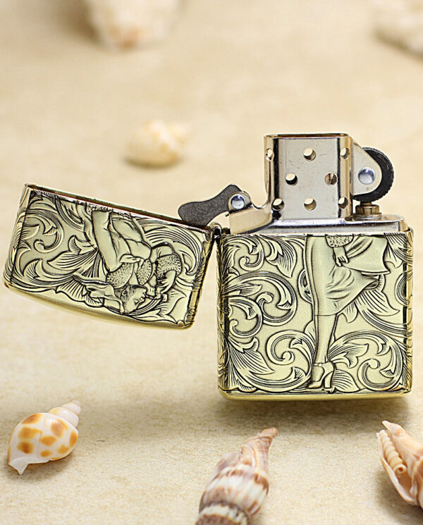 KZ202-02 Ornate metal Zippo-style lighter open on a sandy beach with seashells nearby.