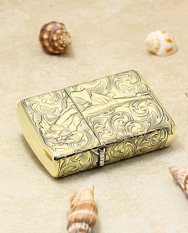 KZ202-04 Golden ornate lighter with swirling engravings on a sandy surface, surrounded by seashells.