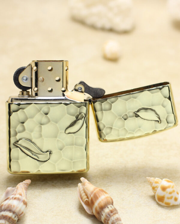 KZ204-03 Gold-toned lighter with pale green reptile-patterned body, open on a sandy beach with seashells nearby.