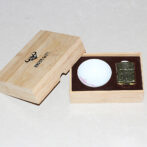 Open wooden box showing a small white ceramic bowl and a gold-tone lighter in a brown foam insert within the box.