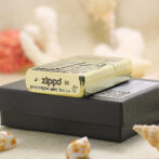 Gold Zippo lighter resting on a black box, with 'Bradford, PA Made in U.S.A.' engraved on the base.