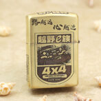 Gold Zippo lighter with a black-and-white 4x4 off-road graphic and Chinese characters, resting on a sandy surface.