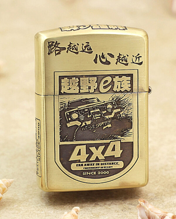 KZ209-01 Gold Zippo lighter with a black-and-white 4x4 off-road graphic and Chinese characters, resting on a sandy surface.