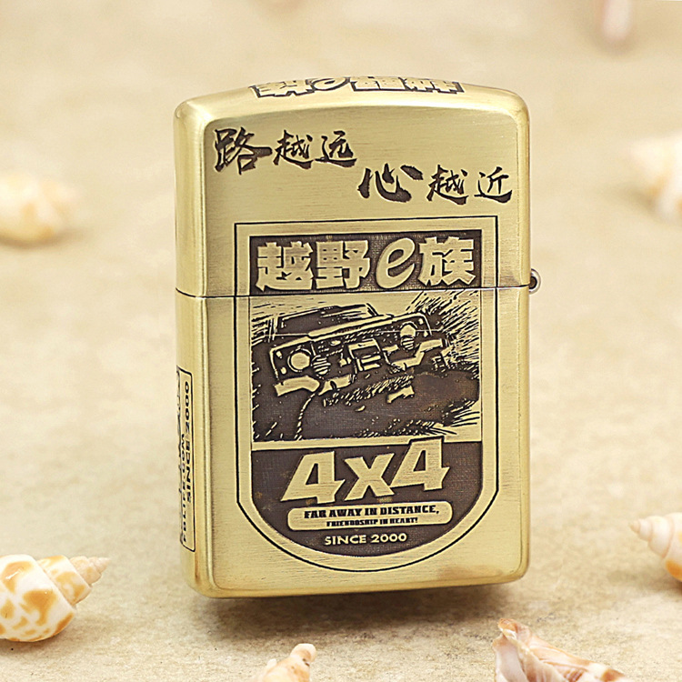Gold Zippo lighter with a black-and-white 4x4 off-road graphic and Chinese characters, resting on a sandy surface.
