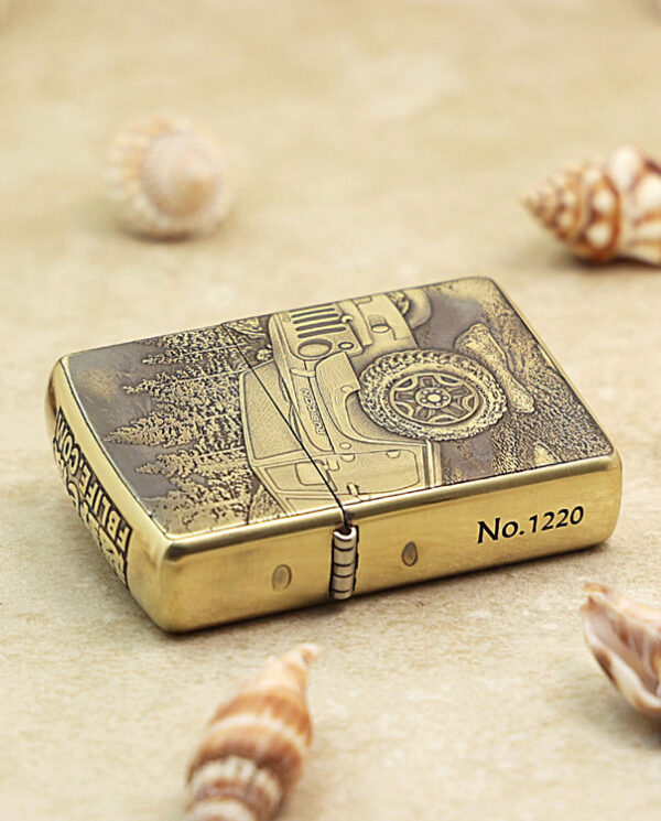 KZ209-04 Brass Zippo-style lighter with a car engraving and winter scene, placed on sandy surface among seashells (No.1220).