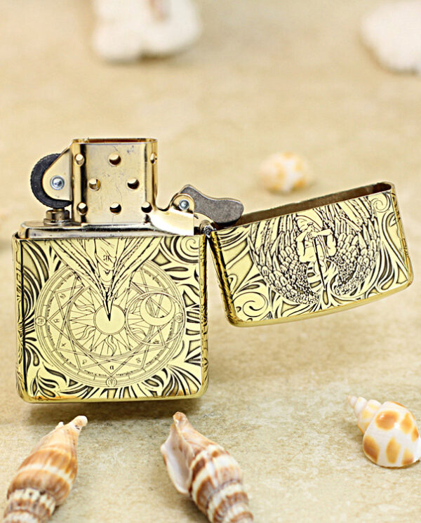 KZ211-03 Decorative gold Zippo lighter with intricate engravings, open, resting on sandy beach with seashells nearby.
