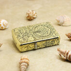 Gold ornate lighter with intricate floral and star designs resting on sandy beach among seashells.