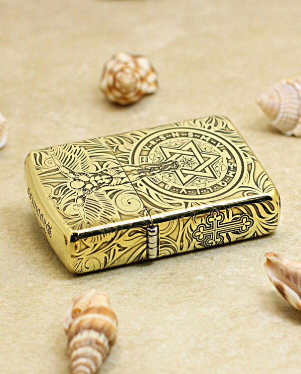KZ211-04 Gold ornate lighter with intricate floral and star designs resting on sandy beach among seashells.
