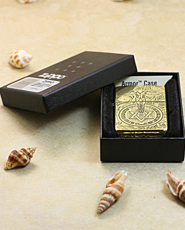 KZ211-06 Gold ornate Zippo lighter in a black presentation box, surrounded by seashells on a beige surface.