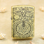 Gold-tone Zippo lighter with black engraving of a winged figure above a circular mystical symbol with a six-pointed star.