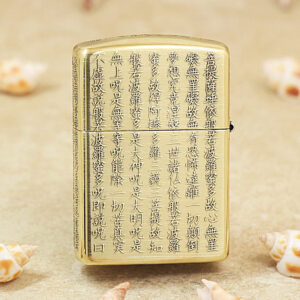 Gold Zippo lighter with vertical Chinese script engraved across its front, set on a sandy surface with small seashells nearby, conveying a decorative, cultural motif.