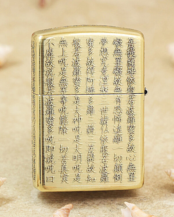 KZ213-01 Gold Zippo lighter with vertical Chinese script engraved across its front, set on a sandy surface with small seashells nearby, conveying a decorative, cultural motif.