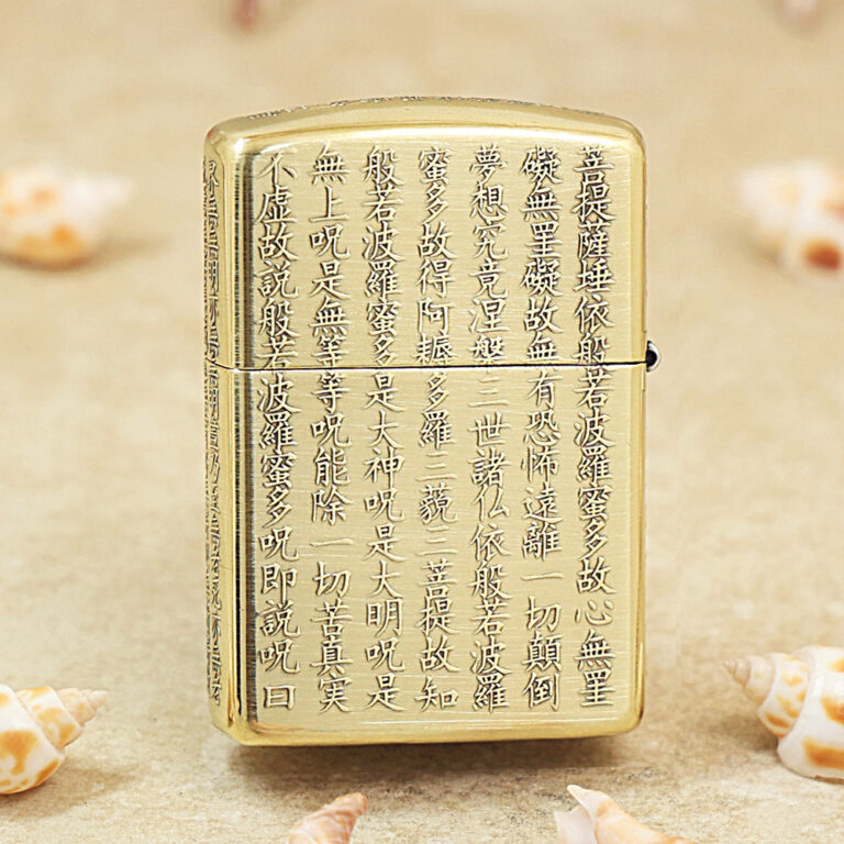Gold Zippo lighter with vertical Chinese script engraved across its front, set on a sandy surface with small seashells nearby, conveying a decorative, cultural motif.
