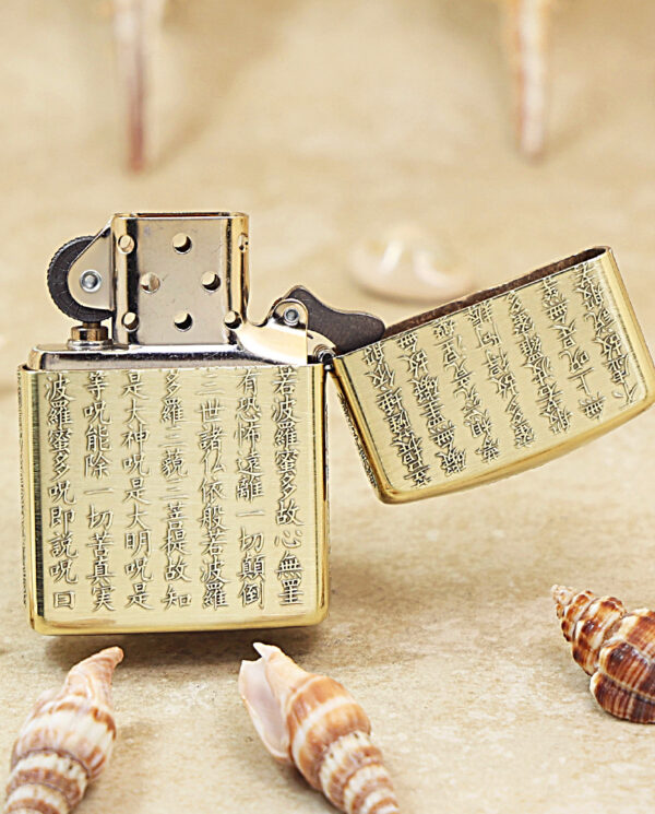 KZ213-03 Brass Zippo lighter with engraved Chinese characters, open lid, surrounded by seashells on a sandy surface