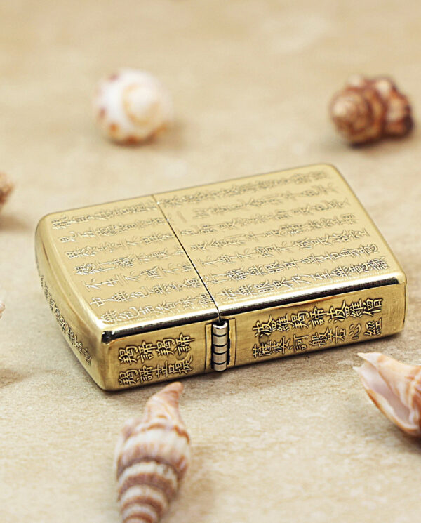 KZ213-04 Gold engraved lighter resting on sand, surrounded by seashells on a beach.
