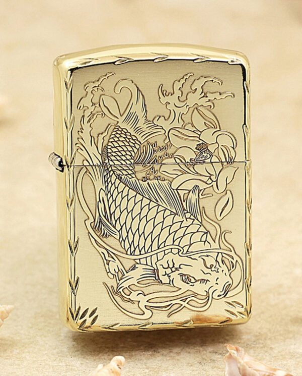 KZ214 Gold metal lighter with an intricate dragon engraving on the front, resting on a sandy surface with seashells nearby.
