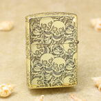 Gold lighter with a raised skulls and roses engraving on a gold surface, decorative pattern across the entire body