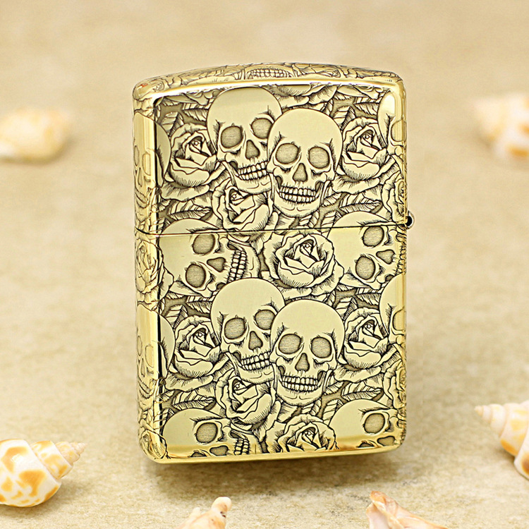 Gold lighter with a raised skulls and roses engraving on a gold surface, decorative pattern across the entire body