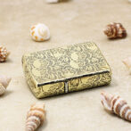 Gold patterned lighter with skulls, placed on sandy surface among seashells.