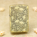 Gold Zippo lighter covered in skull and rose engravings on a sandy surface