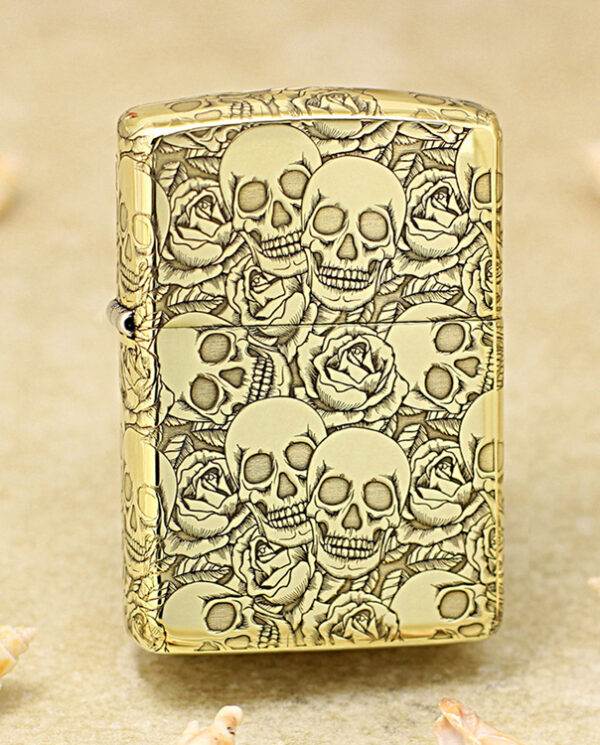 KZ215 Gold Zippo lighter covered in skull and rose engravings on a sandy surface