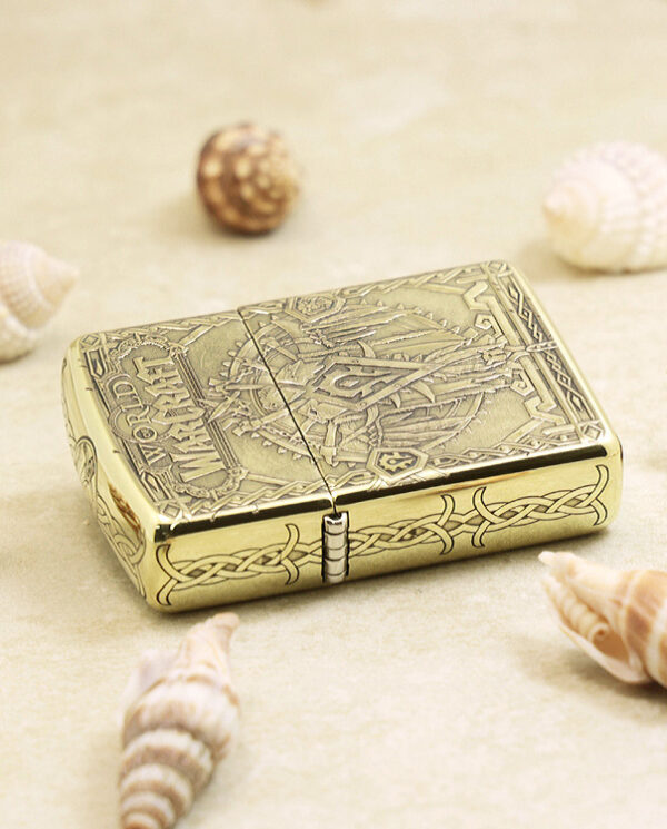 KZ217-04 Gold engraved lighter with Celtic knot patterns on a sandy surface among seashells.