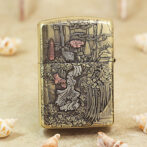 Gold engraved lighter featuring a detailed Asian landscape with pagodas, trees, and flowing water, set on a sandy surface with seashells nearby.