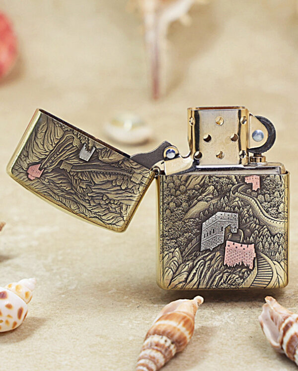 Brass Zippo lighter with intricate engraved landscape, lid open to reveal the mechanism, set among seashells.