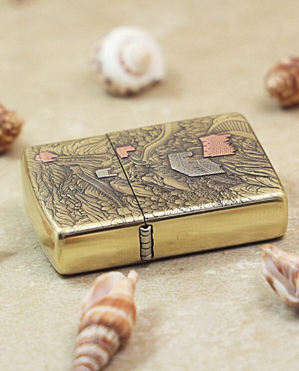 Ornate brass lighter on a sandy surface surrounded by seashells and small shells.
