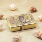 Gold Zippo lighter with a vintage cartoon graphic rests on sand among seashells on a beach.