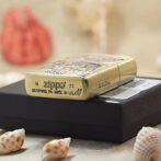 A brass Zippo lighter with engraved patterns rests on a black box, surrounded by small seashells.