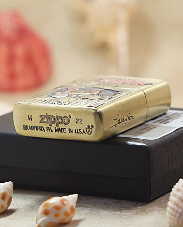 A brass Zippo lighter with engraved patterns rests on a black box, surrounded by small seashells.