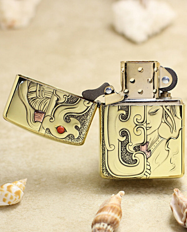 Gold engraved Zippo-style lighter opened on a sandy beach, with seashells around it.