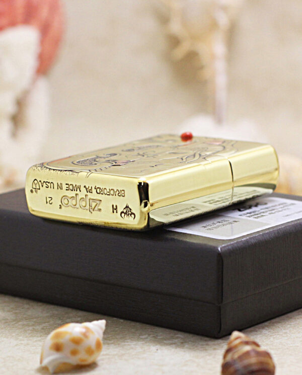 Gold Zippo lighter with decorative engraving on a black presentation box.