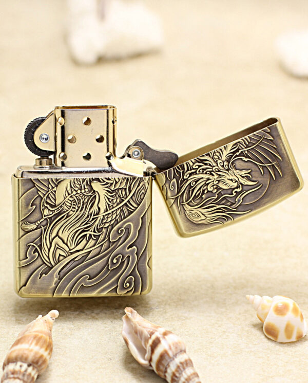 KZ229-03 Brass Zippo-style lighter with a dragon engraving, open lid, on a sandy beach with seashells nearby.