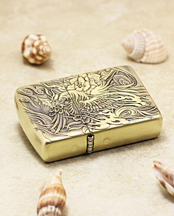 KZ229-04 Brass lighter with intricate dragon engraving, placed on sandy surface among seashells.