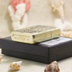 Ornate gold Zippo lighter resting on a dark box with seashells nearby.