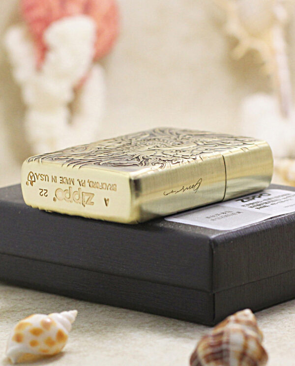 KZ229-05 Ornate gold Zippo lighter resting on a dark box with seashells nearby.