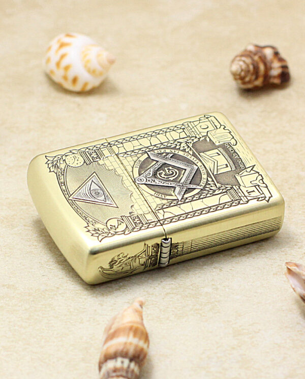 Gold Zippo-style lighter with detailed engravings on a sandy surface among seashells.