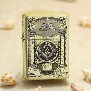 Gold Zippo lighter with Masonic symbols (eye in triangle, compass and square with G) displayed on a sandy beach with seashells nearby.