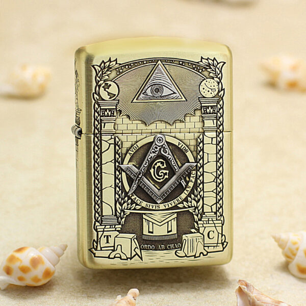 Gold Zippo lighter with Masonic symbols (eye in triangle, compass and square with G) displayed on a sandy beach with seashells nearby.