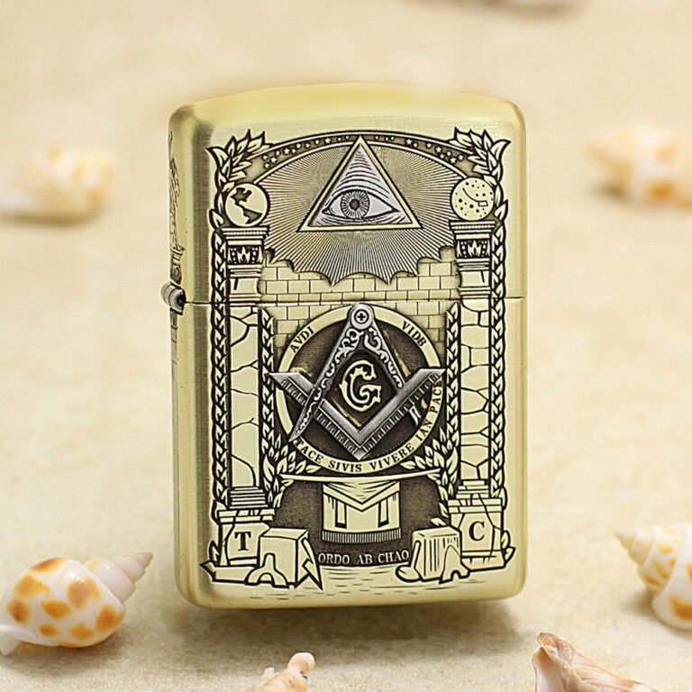 Gold Zippo lighter with Masonic symbols (eye in triangle, compass and square with G) displayed on a sandy beach with seashells nearby.