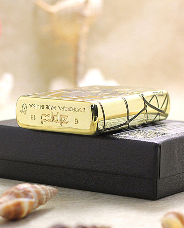 Gold Zippo-style lighter resting on a black box, with seashells and a soft beachy background in view.