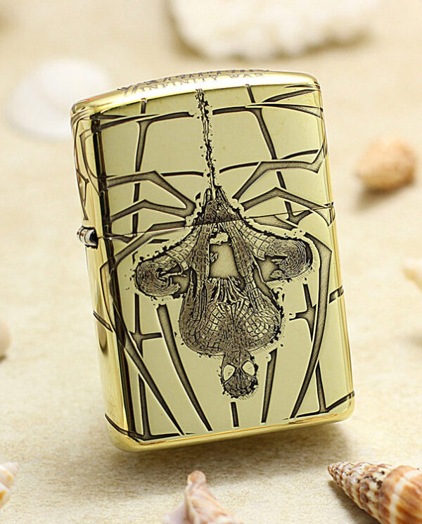 Gold-toned lighter with an ornate skull and geometric engraving, set on a sandy beach with seashells nearby.