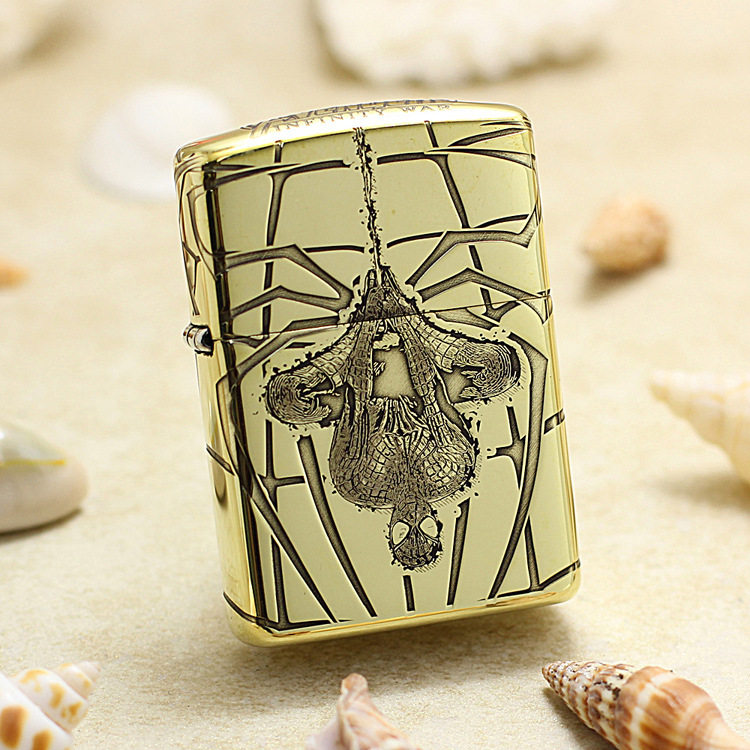 Gold-toned lighter with an ornate skull and geometric engraving, set on a sandy beach with seashells nearby.