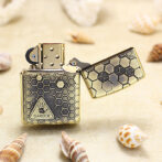 Gold Zippo-style lighter with a black honeycomb hexagon pattern and a triangular 'DANGER' label on the front, open lid.