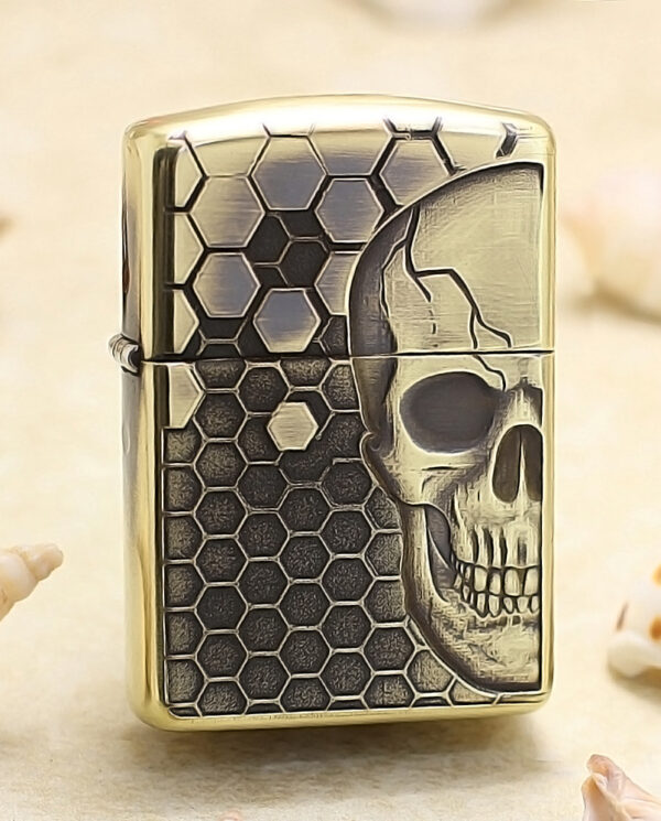 KZ240 Gold-tone lighter with a skull motif over a hexagonal honeycomb pattern, standing upright on a sandy surface.